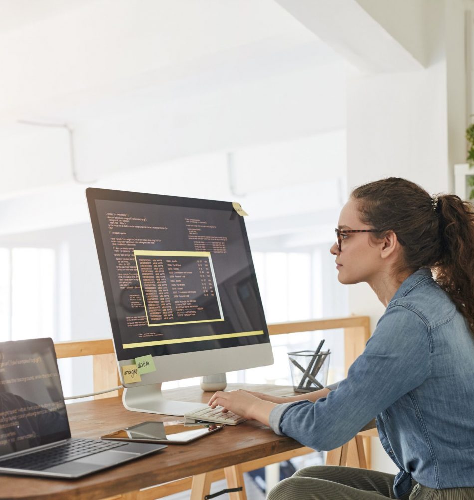 side-view-portrait-female-it-developer-typing-keyboard-with-black-orange-programming-code-computer-screen-laptop-contemporary-office-interior-copy-space (1)