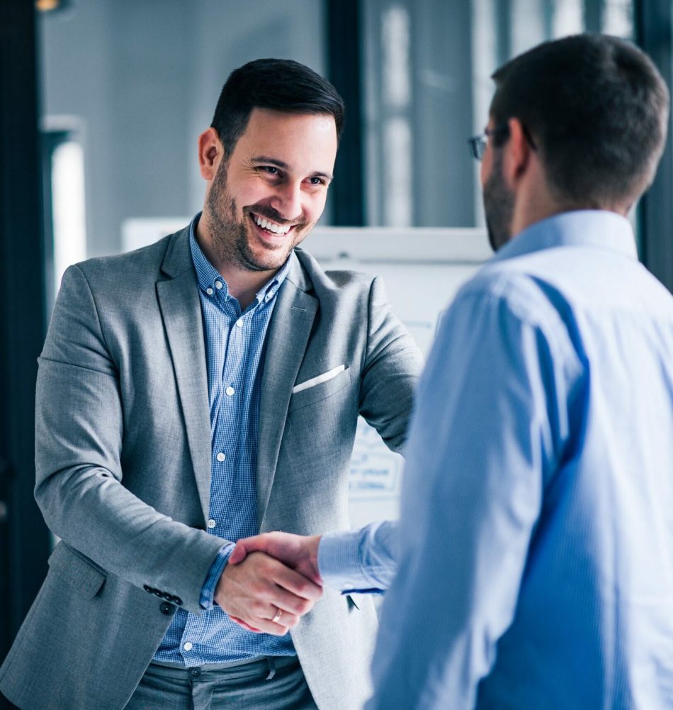 two-smiling-businessmen-shaking-hands-while-standing-office (1)